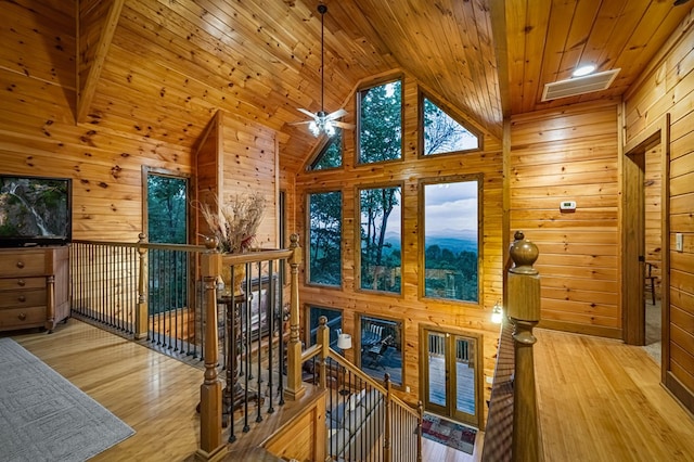 hallway with high vaulted ceiling, wood walls, an upstairs landing, wooden ceiling, and wood finished floors