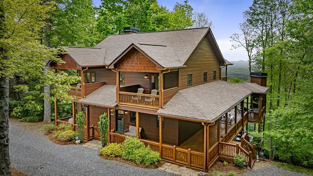 back of house featuring a shingled roof, a chimney, and a balcony