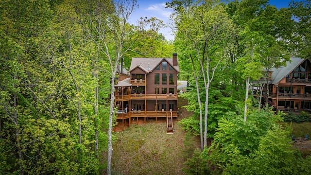 back of house with stairs, a wooden deck, a balcony, and a chimney