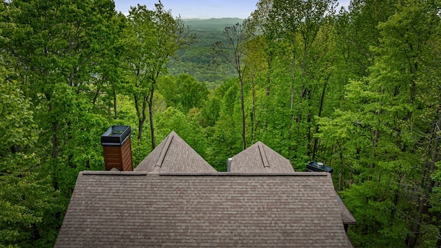 exterior space featuring a shingled roof, a chimney, and a wooded view