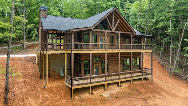 back of house with a wooden deck, a wooded view, a chimney, and roof with shingles