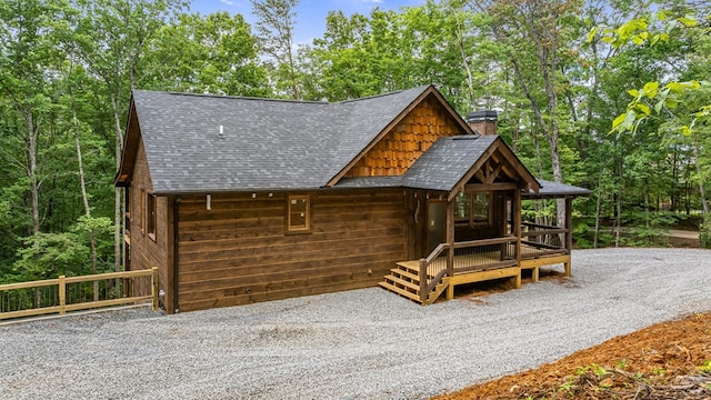 rustic home featuring a wooded view, a chimney, and roof with shingles