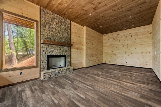 unfurnished living room featuring dark wood finished floors, a stone fireplace, wooden ceiling, and wooden walls