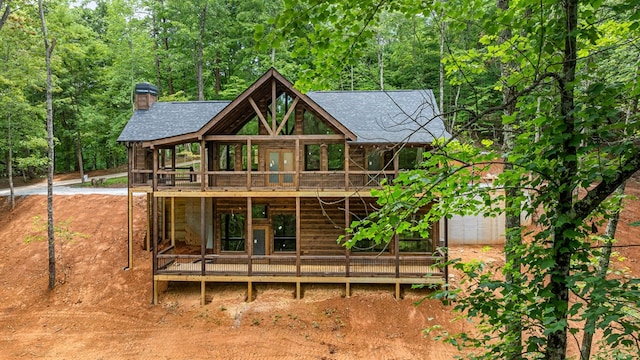 rear view of house featuring a forest view, a wooden deck, and a chimney