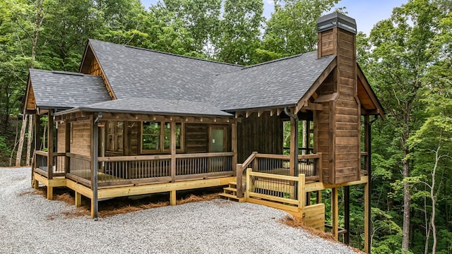 view of front of house with gravel driveway, a chimney, and a shingled roof