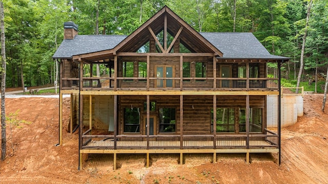 back of house with french doors, a view of trees, and roof with shingles