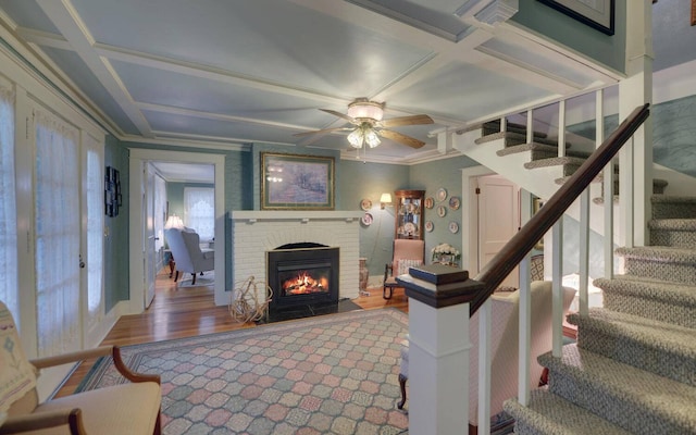 living room featuring coffered ceiling, ceiling fan, crown molding, wood-type flooring, and a fireplace