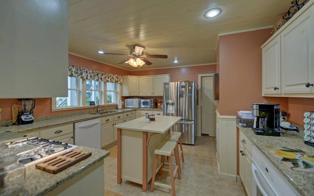 kitchen featuring white appliances, light stone countertops, a kitchen island, white cabinetry, and a breakfast bar area