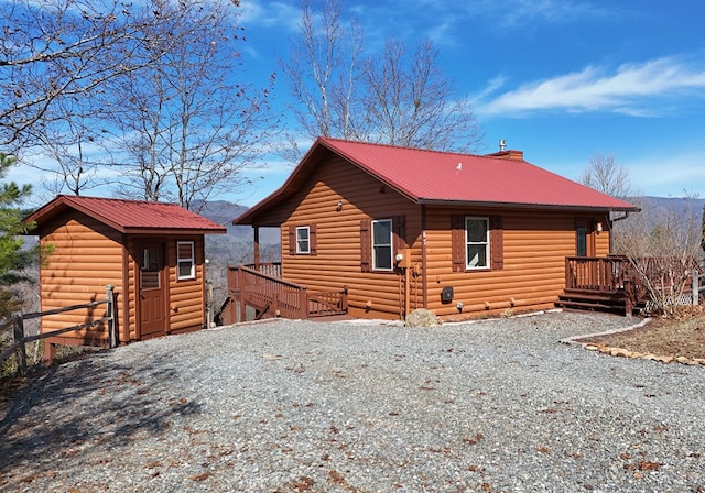 view of side of property featuring an outbuilding, faux log siding, metal roof, and a chimney