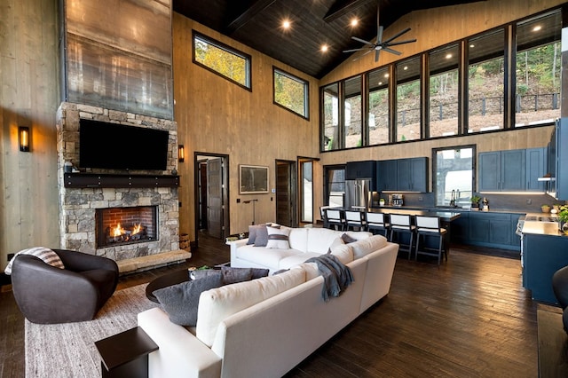 living room featuring high vaulted ceiling, a fireplace, dark wood-type flooring, ceiling fan, and beamed ceiling