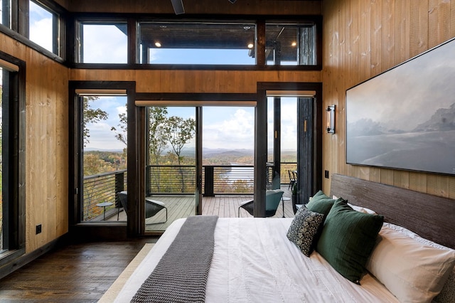 bedroom featuring access to exterior, wood walls, a towering ceiling, and hardwood / wood-style flooring