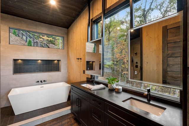 full bathroom featuring wood ceiling, a soaking tub, double vanity, and a sink