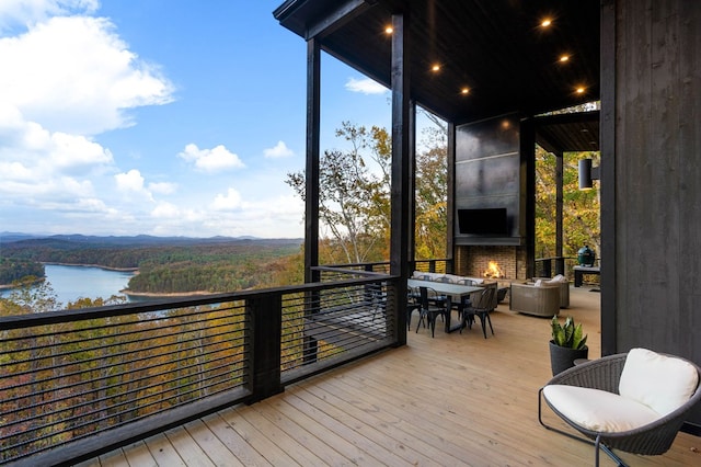 wooden deck featuring a water view, outdoor dining area, and a fireplace