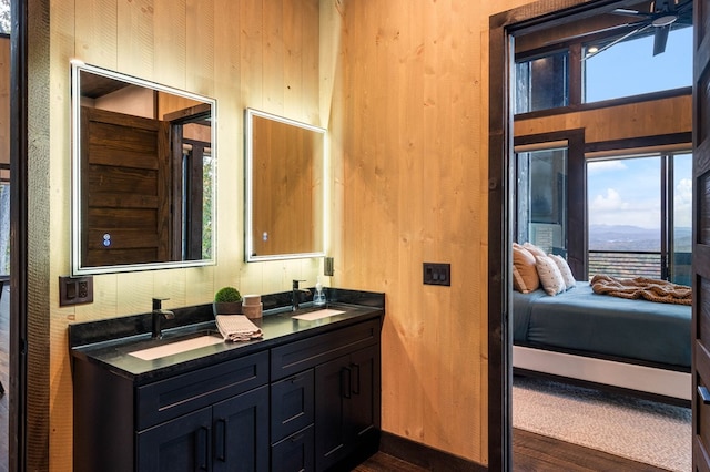 ensuite bathroom featuring connected bathroom, double vanity, a sink, and wood finished floors