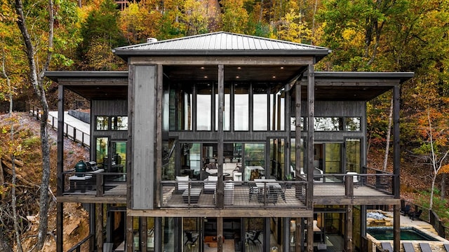 exterior space with a balcony, metal roof, a forest view, and an outdoor pool