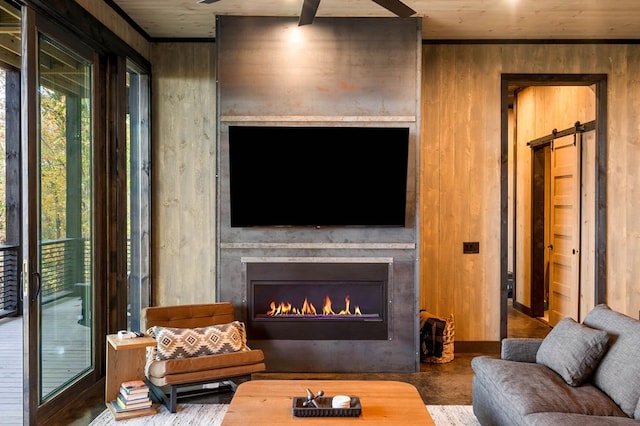 living room featuring a barn door, wooden walls, and a lit fireplace