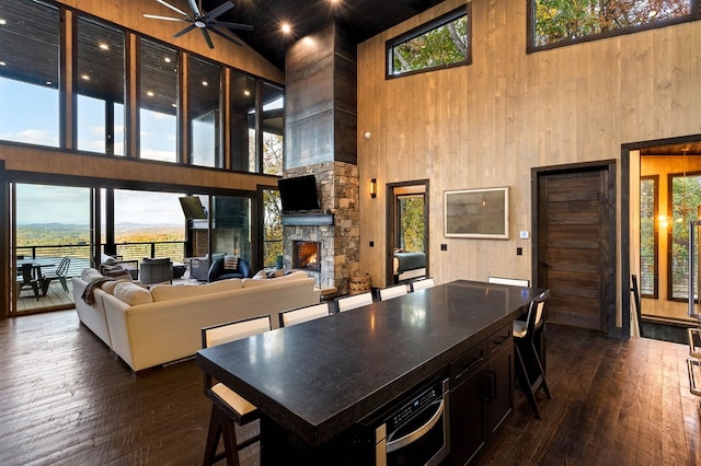 interior space featuring wood walls, dark wood-type flooring, a fireplace, ceiling fan, and a high ceiling