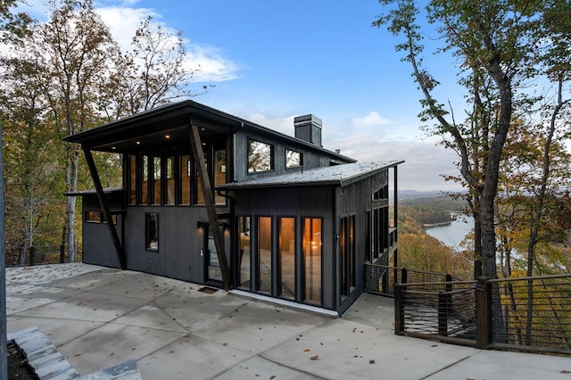 rear view of property featuring a patio area, a water view, and a chimney