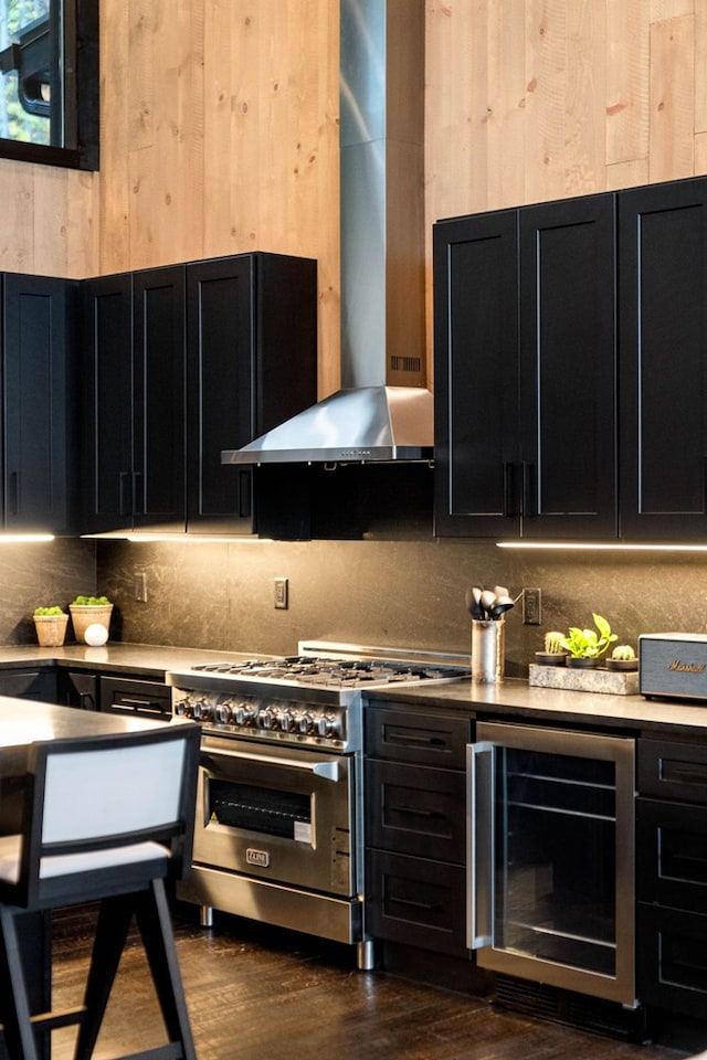 kitchen featuring beverage cooler, dark cabinets, high end range, wall chimney range hood, and tasteful backsplash