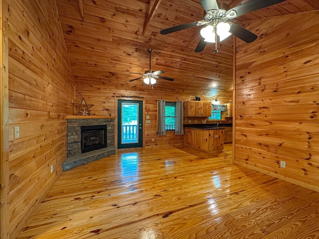 unfurnished living room with a ceiling fan, wood walls, a stone fireplace, light wood-type flooring, and wood ceiling