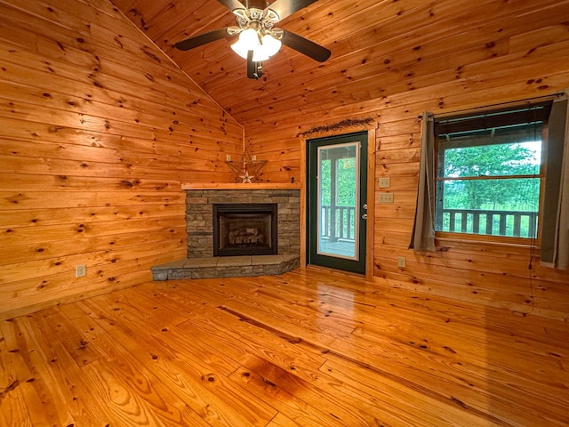 unfurnished living room with a ceiling fan, vaulted ceiling, a fireplace, wood walls, and wood-type flooring