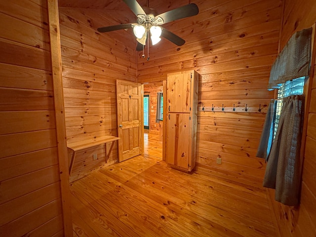 empty room featuring wooden walls, a ceiling fan, and light wood finished floors
