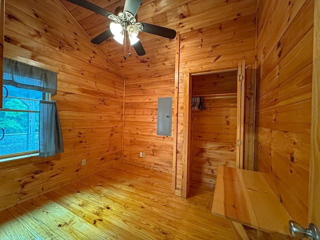 empty room featuring wood walls, lofted ceiling, a ceiling fan, hardwood / wood-style flooring, and electric panel