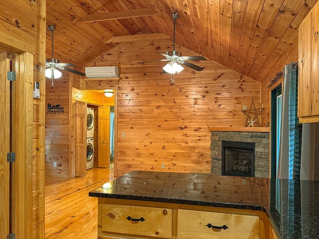 kitchen featuring a ceiling fan, wood walls, stacked washing machine and dryer, vaulted ceiling, and wooden ceiling