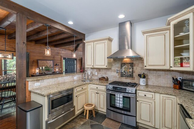 kitchen with beamed ceiling, wall chimney exhaust hood, stainless steel appliances, and cream cabinetry