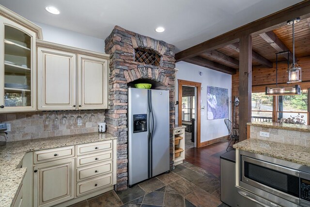 kitchen featuring cream cabinets, beamed ceiling, backsplash, appliances with stainless steel finishes, and light stone counters