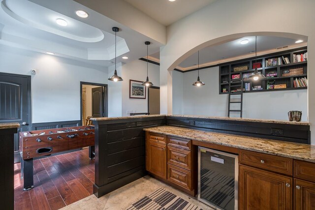 bar featuring light stone countertops, a raised ceiling, hardwood / wood-style floors, decorative light fixtures, and beverage cooler