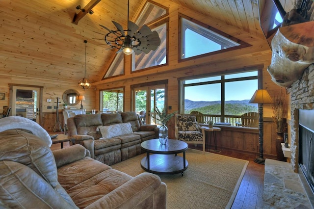 living room with high vaulted ceiling, a mountain view, wooden walls, a stone fireplace, and wood-type flooring