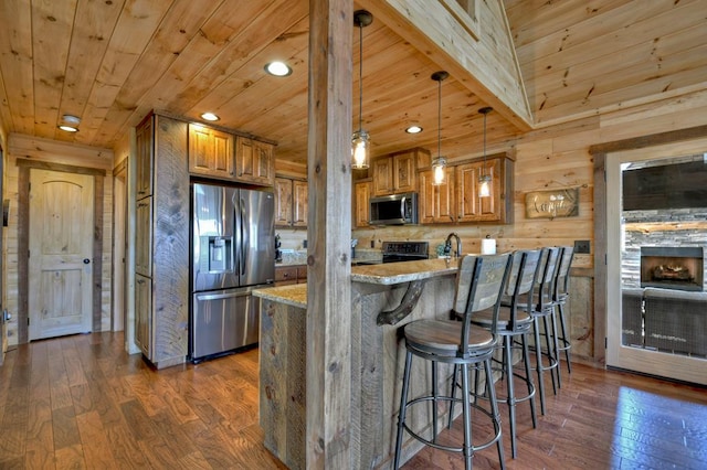 kitchen with light stone counters, dark hardwood / wood-style flooring, stainless steel appliances, wood walls, and decorative light fixtures