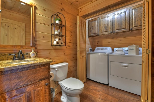 laundry area featuring sink, dark wood-type flooring, wood walls, and separate washer and dryer