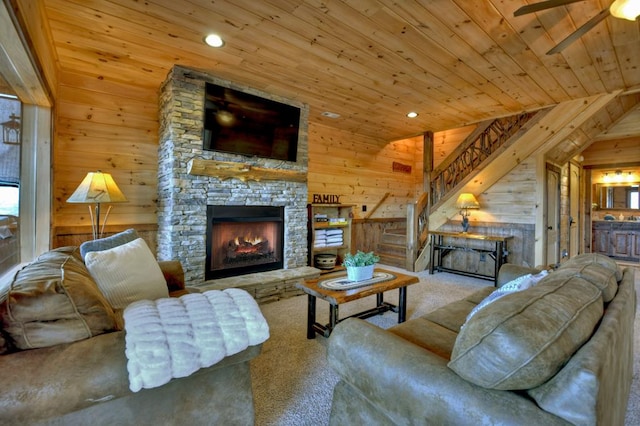 carpeted living room featuring wood walls, a fireplace, vaulted ceiling, ceiling fan, and wood ceiling