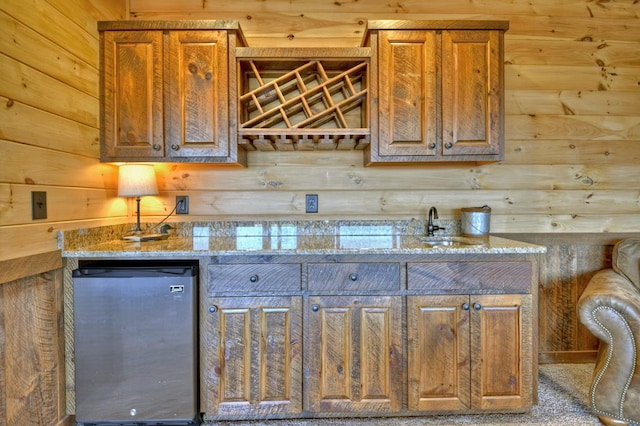 kitchen featuring light stone countertops, log walls, sink, and fridge