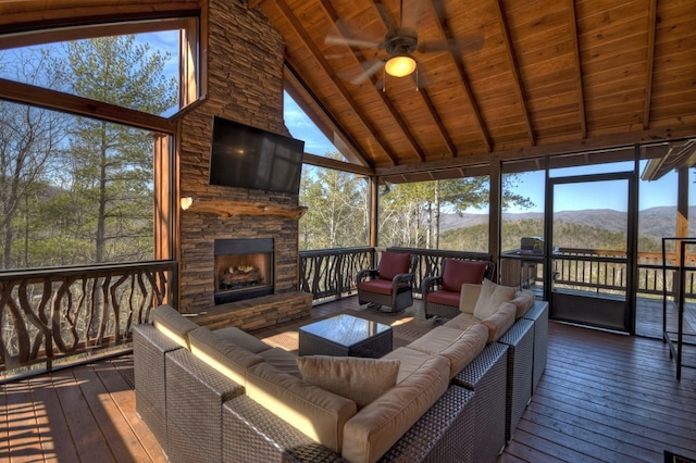 sunroom featuring wooden ceiling, a stone fireplace, a mountain view, ceiling fan, and lofted ceiling with beams