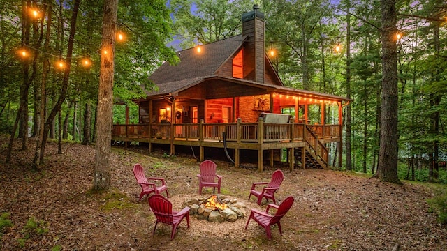 rear view of property featuring stairs, a wooden deck, a chimney, and an outdoor fire pit