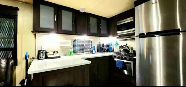 kitchen featuring stainless steel appliances, light countertops, glass insert cabinets, and dark brown cabinets