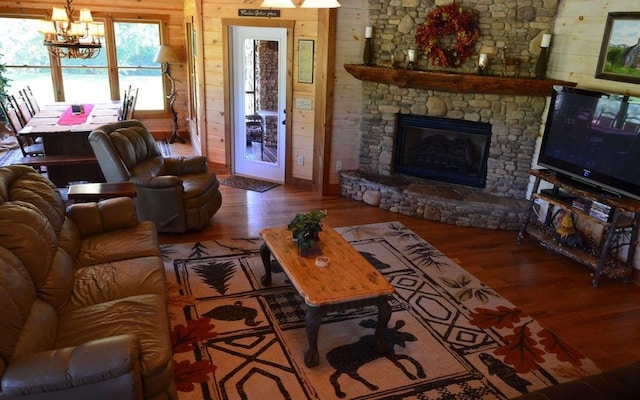 living room with a stone fireplace, an inviting chandelier, wooden walls, and hardwood / wood-style floors