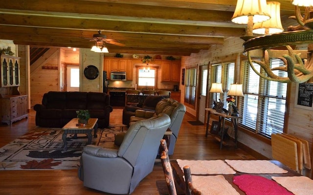 living room with wood walls, dark wood-type flooring, ceiling fan, and beam ceiling