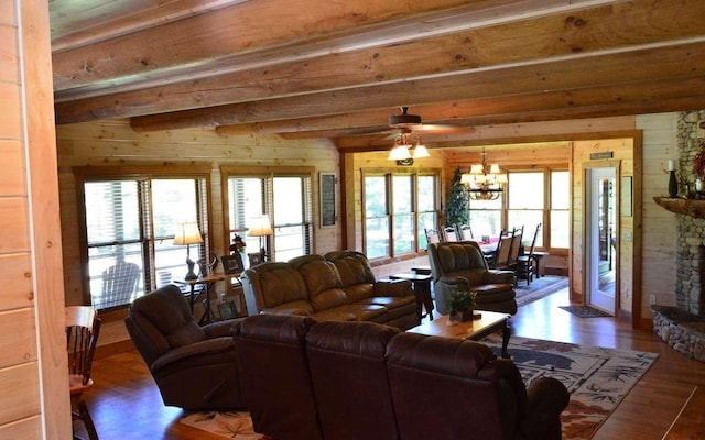 living room with lofted ceiling with beams, a stone fireplace, dark hardwood / wood-style floors, wooden walls, and ceiling fan with notable chandelier