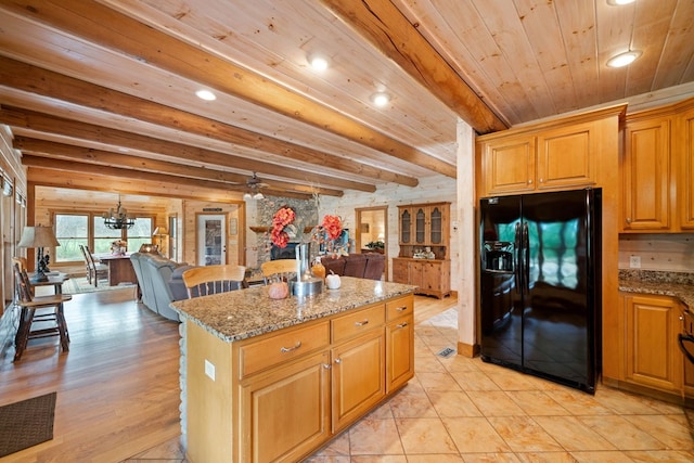 kitchen featuring black refrigerator with ice dispenser, light stone countertops, beam ceiling, light hardwood / wood-style flooring, and a kitchen island