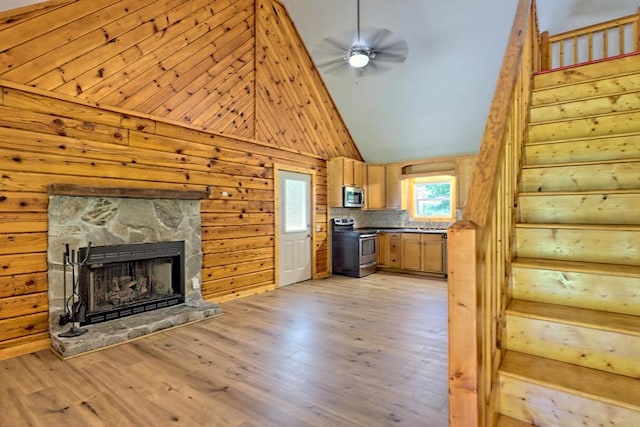 kitchen with backsplash, stainless steel appliances, high vaulted ceiling, light hardwood / wood-style floors, and a stone fireplace