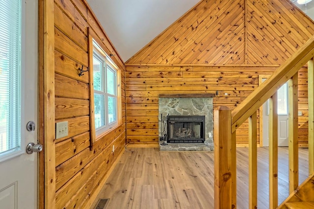 unfurnished living room featuring a stone fireplace, wood walls, plenty of natural light, vaulted ceiling, and light wood-type flooring