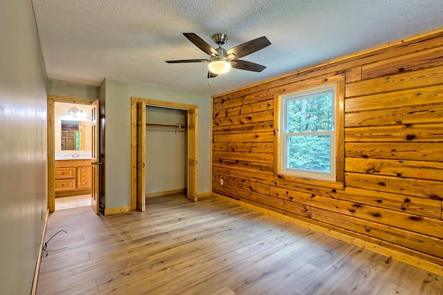 unfurnished bedroom with wooden walls, ensuite bath, ceiling fan, light hardwood / wood-style floors, and a closet