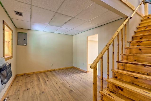 basement with a paneled ceiling, electric panel, light hardwood / wood-style flooring, and heating unit