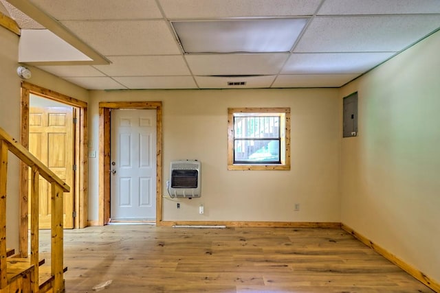 empty room with light wood-type flooring, heating unit, a drop ceiling, and electric panel