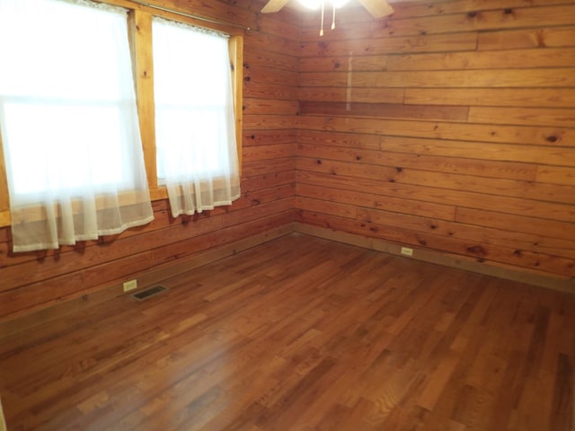 unfurnished room with a ceiling fan, visible vents, wooden walls, and wood finished floors