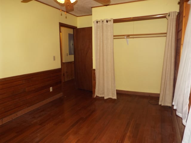 unfurnished bedroom with electric panel, wooden walls, dark wood finished floors, ceiling fan, and a closet